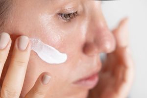 O femeie cu ten mixt sau gras care aplica un produs cu SPF pe fata