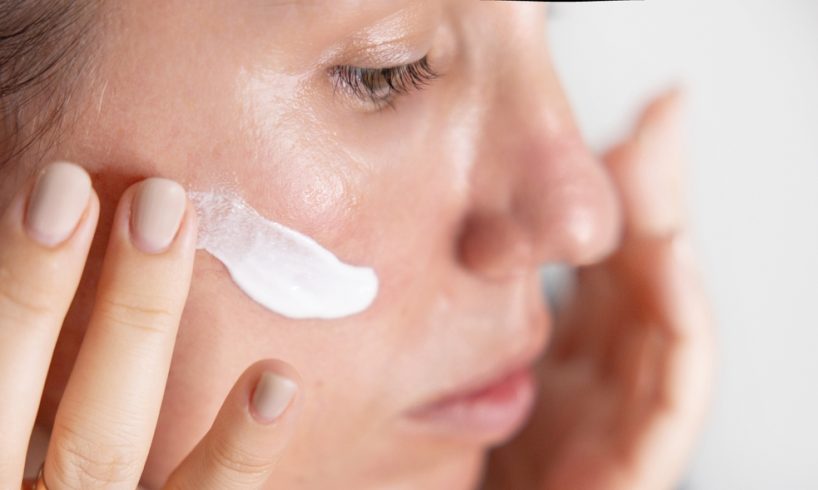 O femeie cu ten mixt sau gras care aplica un produs cu SPF pe fata